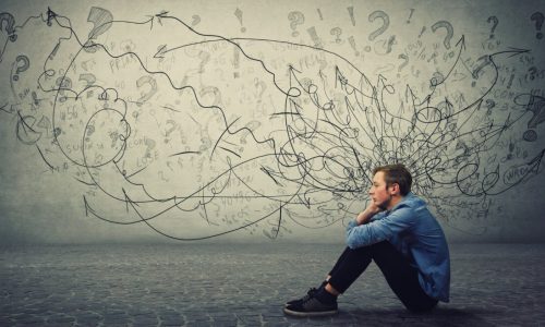 Upset and tired boy teenager sitting on the floor keeps hand to cheek looking thoughtfully and hopeless. Stressed student guy feels emotional discomfort, anxiety and mental health problems.